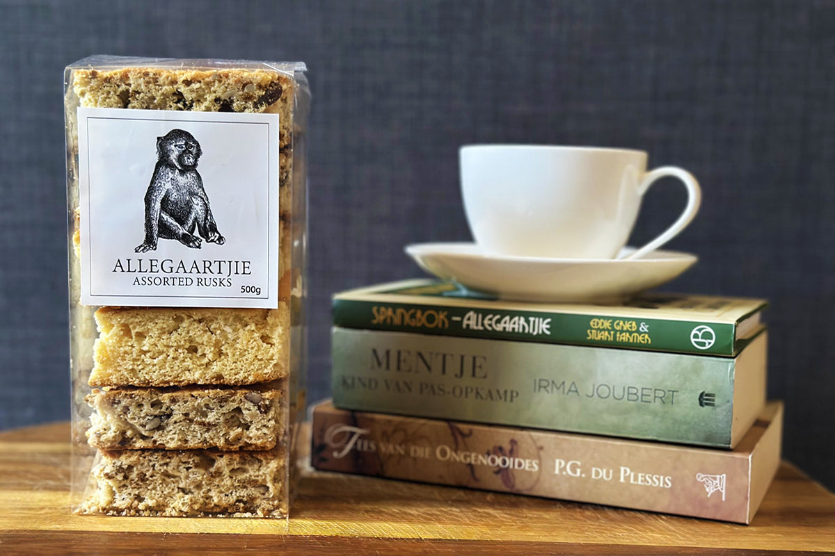 Assorted South African-style rusks arranged on a wooden board – including buttermilk, nutty bran, muesli, and malva pudding varieties – served with a cup of tea.